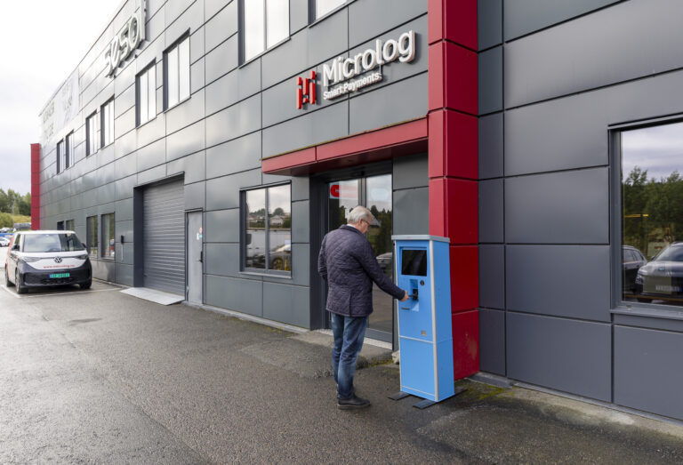 Mann som står utenfor Micrologs kontorer og bruker parkeringsautomaten til Microlog